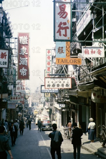 Busy street of shops and signs in English and Mandarin including for Tai Cheong Tailors, Wellington Street, Hong Kong, Asia 1964.