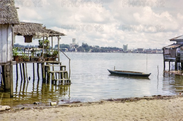 View across Straits from coastal village Kampong Lorong Fatimah in Singapore to Johor Bahru, Malaysia, Southeast Asia c 1964.