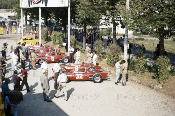 Ferrari Formula One team in paddock with sharknose Ferrari 156 F1 cars, Ferraris, Monza Grand Prix, Italy 1961 thought to be Baghetti chatting with a mechanic right side.