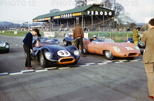 John Coundley (32) brown Jaguar E-type car and Bill de Selincourt (33), Jaguar Lister 'Knobbly' car, Sports car racing Goodwood, March 1961 on the start start line.