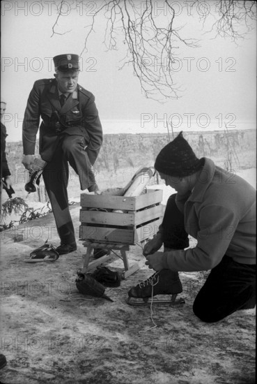 Policeman and man pulling on ice skates, 1963