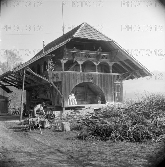 Man bundling firewood in front of a granary in Wynigen BE 1960