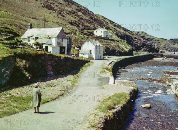 Road passing historic buildings by harbour wall fishing village of Boscastle.