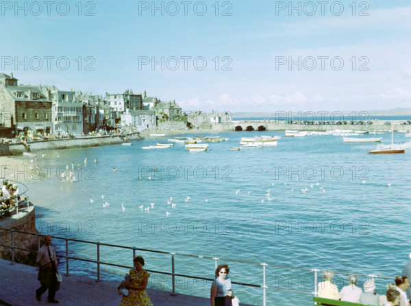 Boats at moorings in the harbour people swimming in sea from beach at St Ives.