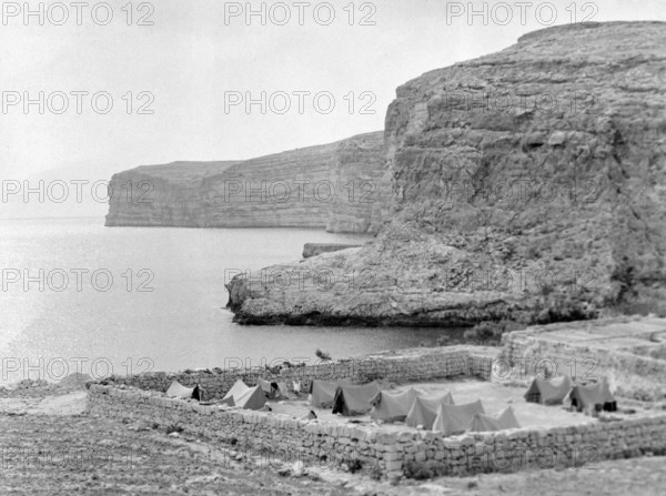 Military tents at walled campsite overlooking sea cliffs at Xlendi Bay.