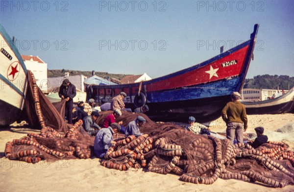 Fishermen repairing nets on beach by traditional fishing boats.