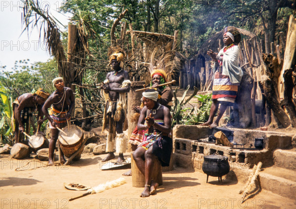 group of Zulu people dressed in traditional attire, performing an outdoor ceremony at a village, likely in the KwaZulu-Natal province of South Africa.