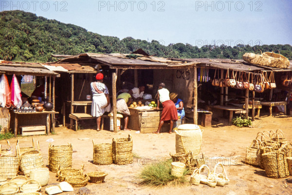 Woman at local market selling fruit and handicrafts including baskets.