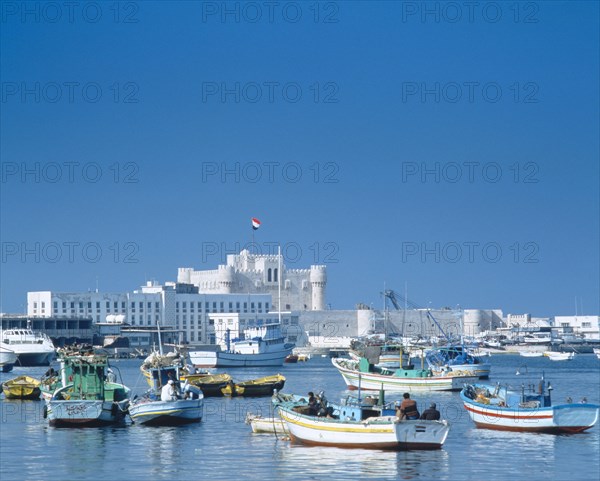 EGYPT, Nile Delta, Alexandria, Fishing boats moored in harbour with fortress castle and walls beyond.