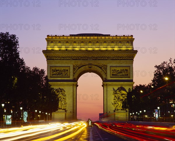 FRANCE, Ile de France, Paris, Arc de Triomphe at night with light trails from passing cars.