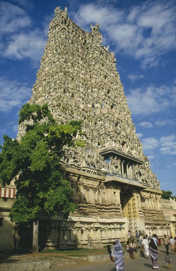 INDIA, Tamil Nadu, Madurai, Sri Meenakshi Temple pyramidal tower or gopuram with people walking towards the entrance