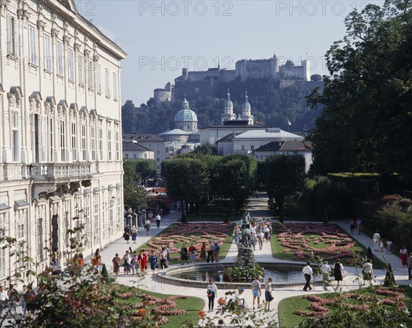 AUSTRIA, Salzburg Province, Salzburg, Mirabell Palace with tourists walking in the formal gardens with Hohensalzburg Fortress on the overlooking hill