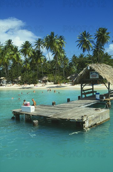 WEST INDIES, Tobago, Pigeon Point, Boat jetty with tourist sitting down and the beach behind with people swimming and sunbathing