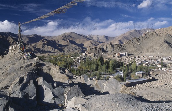 INDIA, Ladakh, Leh, Prayer flags blowing in the wind on top of rocks in the foreground overlooking town surrounded by mountains