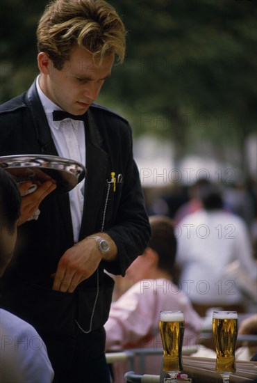FRANCE, Ile de France, Paris, Formal waiter standing at a table with drinks on and holding a silver tray