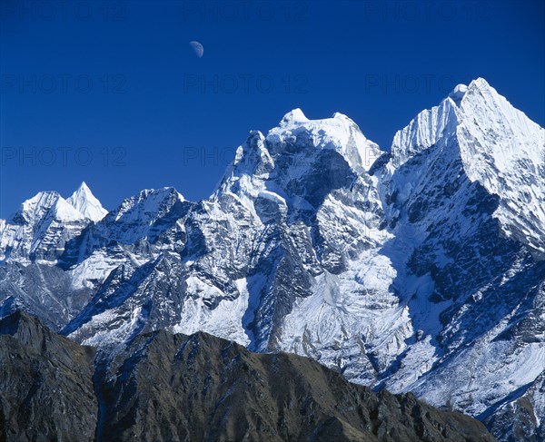 NEPAL, Sagarmatha National Park, Himalayan mountain peaks with moon above just visible in deep blue sky.