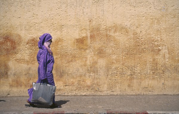 MOROCCO, Traditional Clothing, Woman with veil waliking past colourful wall.