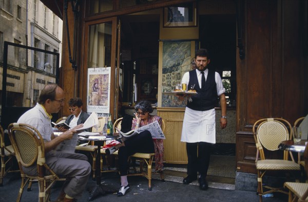 FRANCE, Ile de France, Paris,  A waiter carrying a tray with drinks to customers sat outside la Palette Cafe.