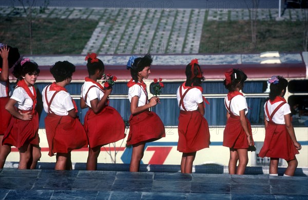 CUBA, Santa Clara, School children wearing red and white uniforms standing in line with some holding red roses