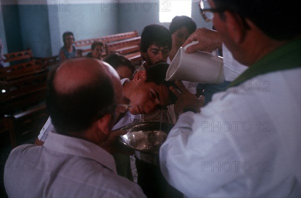 CUBA, Guimero , Man having holy water poured over his head by a priest at an adult Christening service
