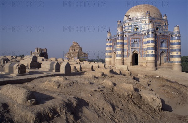 PAKISTAN, Uch Sharif, Tomb of Bibi Jawindi with domed roof and two similar crumbling buildings with dusty graveyard in the foreground