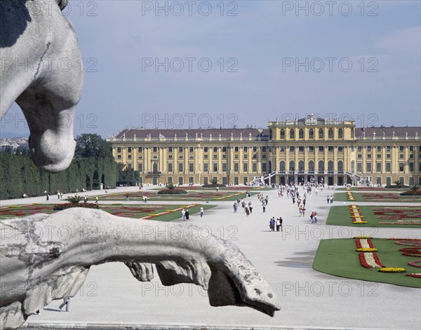 AUSTRIA, Lowe Austria, Vienna, Schonbrunn Palace and tourists walking in the formal gardens with a stone equestrian statue in the foreground