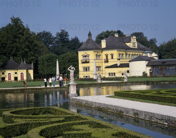 AUSTRIA, Salzburg Province, Salzburg, "Hellbrunn Palace, a yellow building behind an ornamental lake rimmed with boxed hedges "