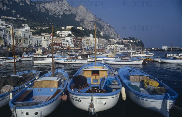 ITALY, Campania, Capri, Marina Grande. Moored boats on water with waterside buildings overlooked by mountains