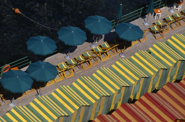 ITALY, Campania, Sorrento, "View over green and yellow and red and yellow striped beach huts, green and yellow striped deck chairs and green sun umbrellas on wooden decking."