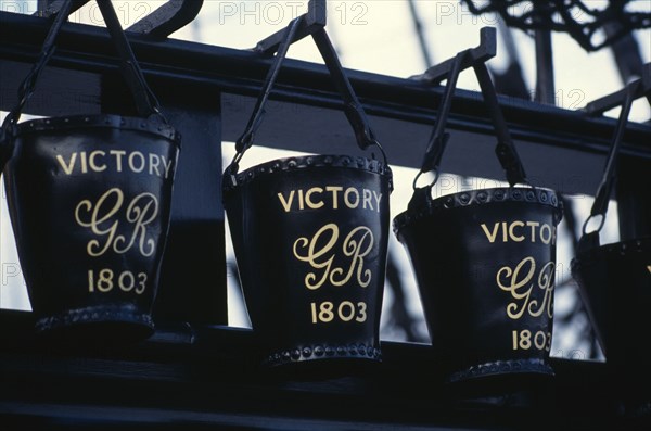 ENGLAND, Hampshire, Portsmouth, HMS Victory.  Detail of black leather buckets hanging from row of metal hooks.