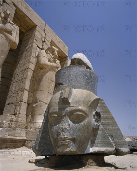 EGYPT, Nile Valley, Thebes, "The Ramesseum, large fallen carved stone head of Ramses II at foot of the remains of Osiride Columns which depict Ramses as Osiris, god of the underworld."