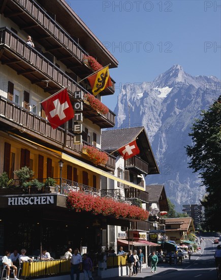 SWITZERLAND, Bern Oberland, Grindelwald, Main street and hotel e distance with flags on the balconies and a snowcapped mountain