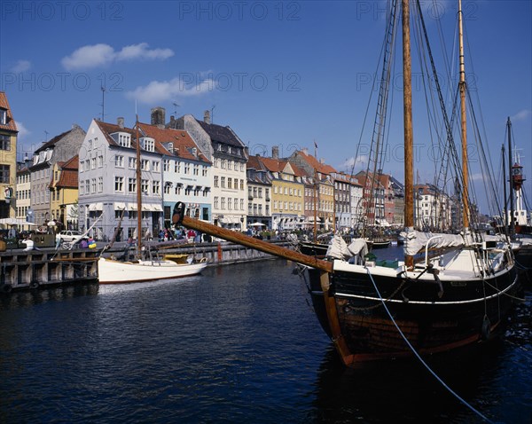 DENMARK, Zealand, Copenhagen, Nyhavn harbour. Traditional waterfront buildings with moored boats and a schooner in the foreground