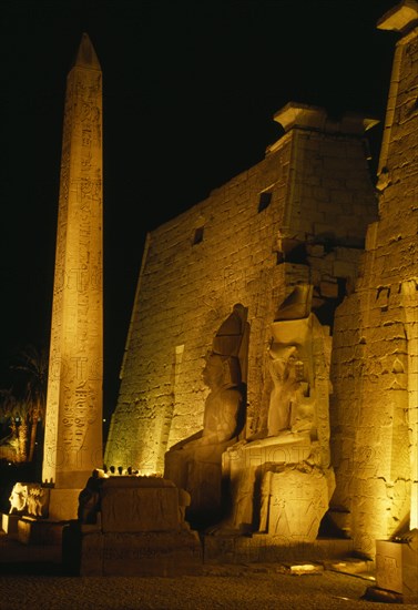 EGYPT, Luxor, The temple illuminated at night seated statues of Ramesses II outside the Pylon with the Obelisk