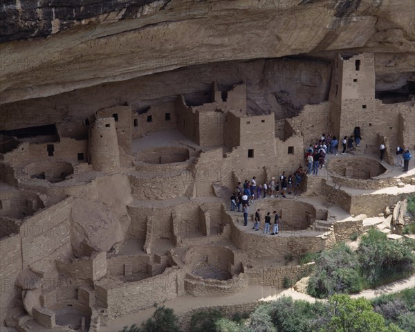 USA, Colorado, Mesa Verde National Park, Cliff Palace the preserved ruins and cave houses beneath rock face. Visitors walk through site of walls and towers with circular foundations leading to deeper caves.