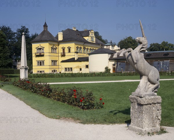 AUSTRIA, Salzburg Province, Salzburg, "Hellbrunn Palace, yellow building seen from across gardens with a unicorn statue in the foreground"
