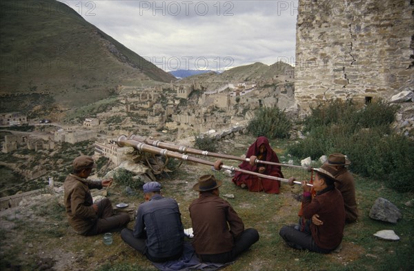 CHINA, Tibet, Ganden, Men blowing long horns on a hillside at Ganden Monastery