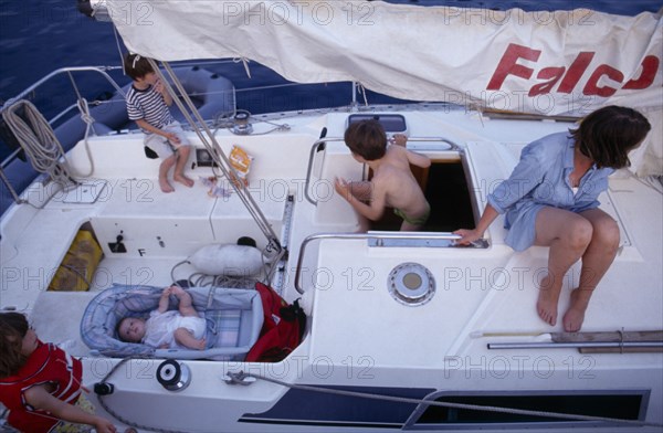 10031035 LEISURE Sailing Yachting Greece. View over a family on a sailing holiday aboard their yacht. Mother with children and a baby lying in a carry cot