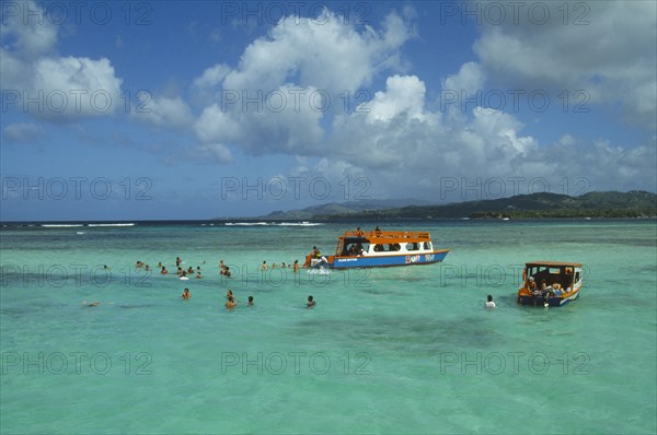 WEST INDIES, Tobago, Buccoo Reef, Nylon Pool with tourists swimming or standing in shallow water by boats