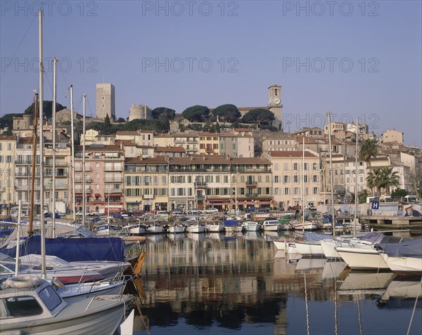 FRANCE, Provence Cote d’Azur, Alpes Maritime, Cannes castle above the harbour buildings with boats moored in the foreground
