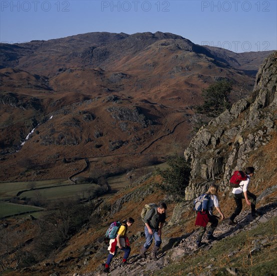 ENGLAND, Cumbria, Lake District, Walkers on footpath to Helm Crag above Grasmere with view west to Sour Milk Gill.