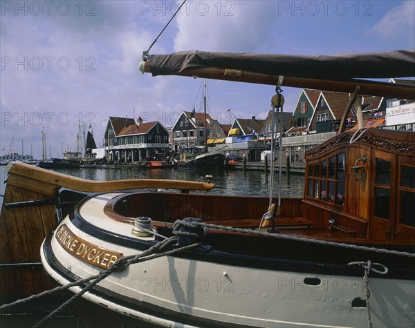 HOLLAND, North, Volendam, Harbour and buildings with many boats moored seen across the stern of a sailing barge