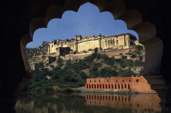 INDIA, Rajasthan, Amber, Amber Palace Fort near Jaipur situated on hillside above lake framed by scalloped edge of silhouetted window.