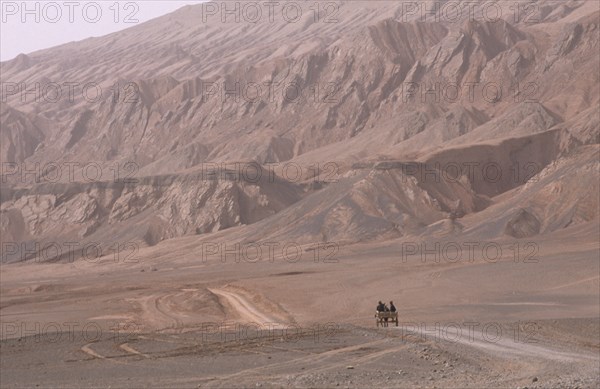 CHINA, Xinjiang, Near Turfan, Desert landscape with horse drawn cart heading along dusty track