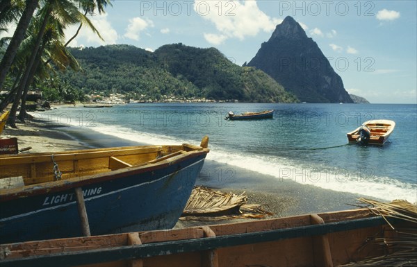 WEST INDIES, St Lucia, Soufriere, Stretch of sandy beach with boats moored in the foreground and the Pitons beyond.