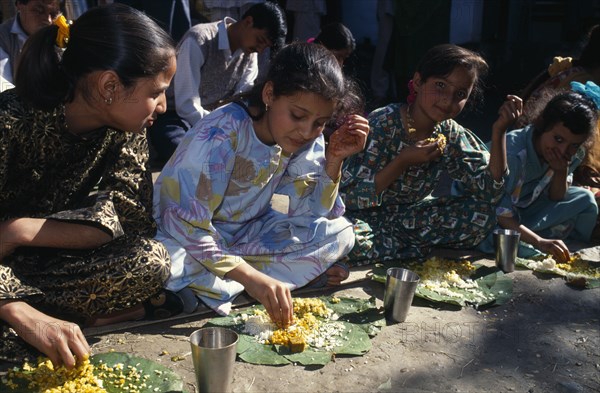 INDIA, Himachal Pradesh, Kulu, Girls eating from banana leaves with their hands at meal during country wedding.