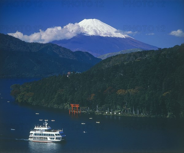 JAPAN, Honshu, Ashino Lake, Mount Fuji with snow cap above the lake with a passenger boat passing the Hakone torii gate