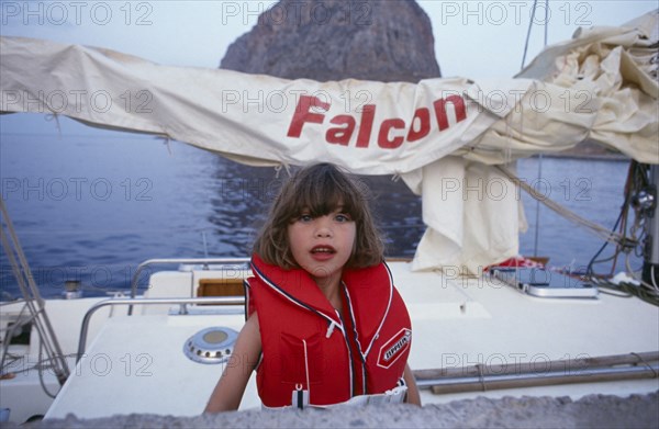 10045186 CHILDREN Leisure Yachting Greece. Monemvasia. An English family on a sailing holiday aboard their yacht with a young girl wearing a life jacket