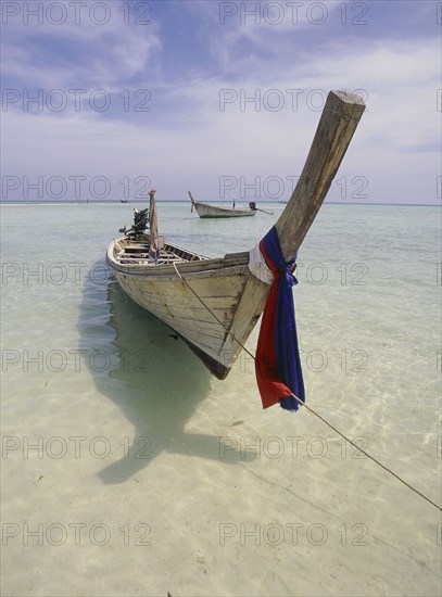 THAILAND, Krabi, Phi Phi Don, Lobagao Bay on the north of the island. Longtail boat moored off the beach with a reflection on the water forming a shape of a fish.