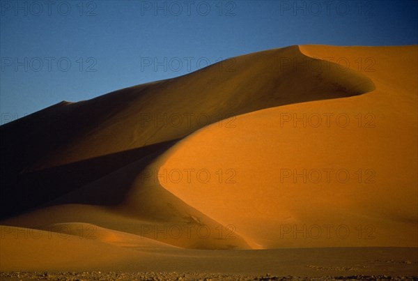 LIBYA , South West, Achan , Orange desert sand dunes partially cast in shadow against a clear blue sky